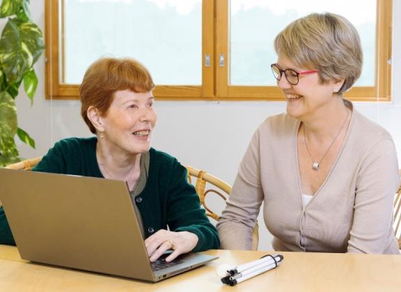 Kaksi naista pöydän ääressä, toisen edessä kannettava tietokone.